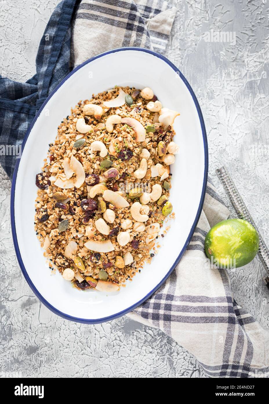 Un plateau blanc métallique rempli de délicieux granola sur une serviette rustique sur un fond blanc et gris à côté d'une lime râpée et d'un râpe. Banque D'Images