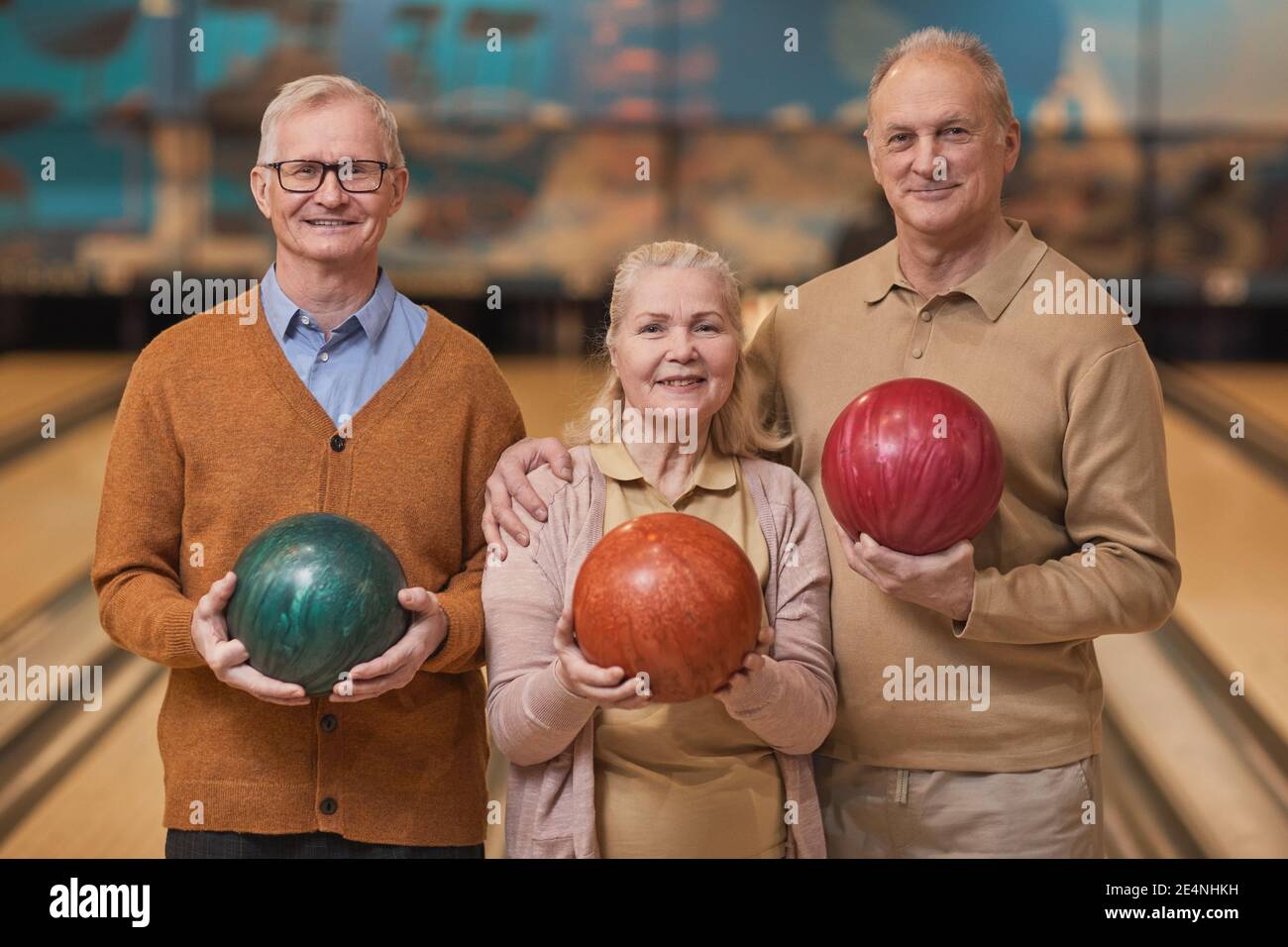 Portrait de trois personnes âgées souriantes tenant des boules de bowling et regardant l'appareil photo tout en appréciant les divertissements actifs à la piste de bowling, cop Banque D'Images