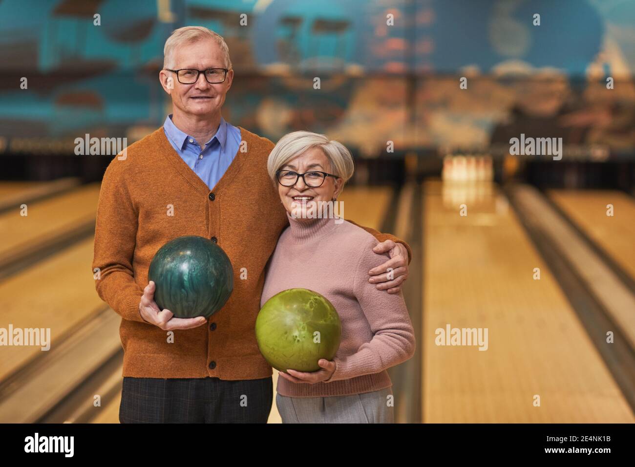 Portrait d'un couple senior heureux tenant des boules de bowling et souriant à l'appareil photo tout en appréciant les divertissements actifs à la piste de bowling, espace de copie Banque D'Images