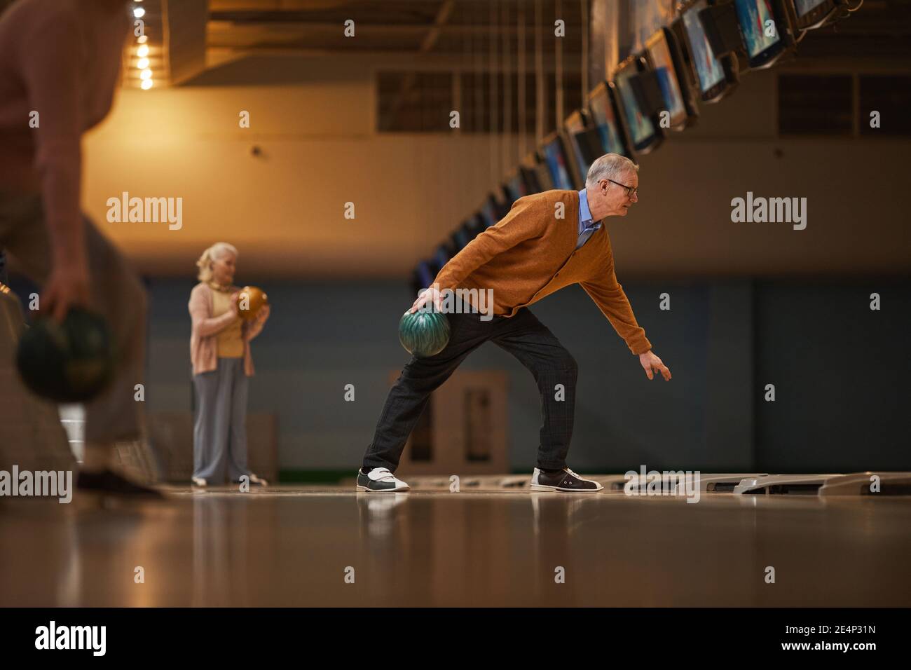 Vue latérale grand angle sur les personnes âgées jouant au bowling tout en appréciant les divertissements actifs à la piste de bowling, l'espace de copie Banque D'Images