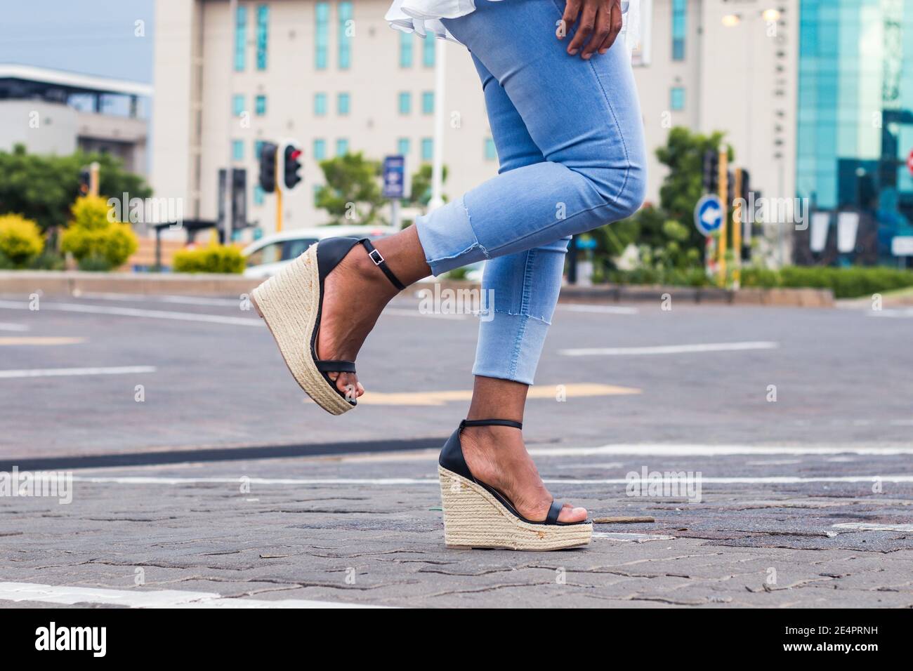 Femme en Jean bleu élégant et sandales à talons compensés avec 1 jambe relevée dans la rue de la ville. Banque D'Images