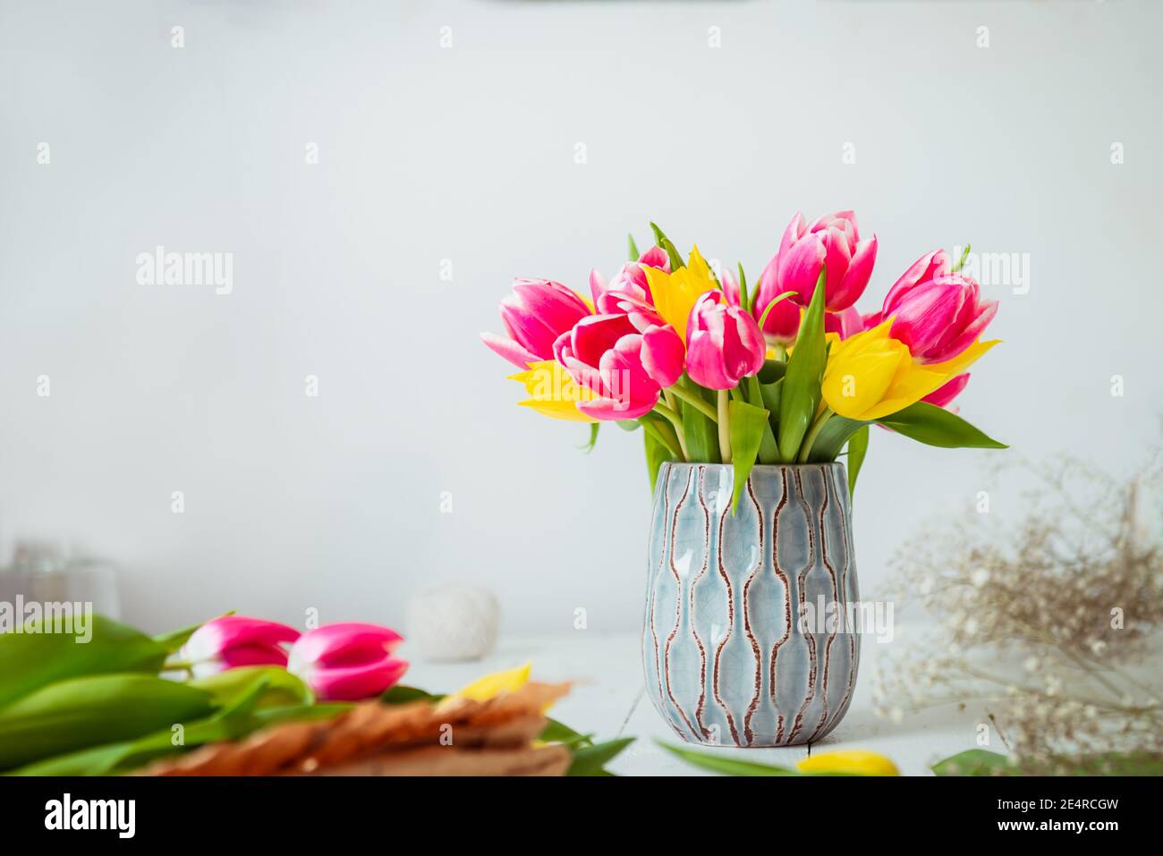 Bouquet de tulipes jaunes et roses dans un vase, autres fleurs et détails sur l'espace de travail des fleuristes sur une table en bois blanc. Éducation de la floristerie Banque D'Images