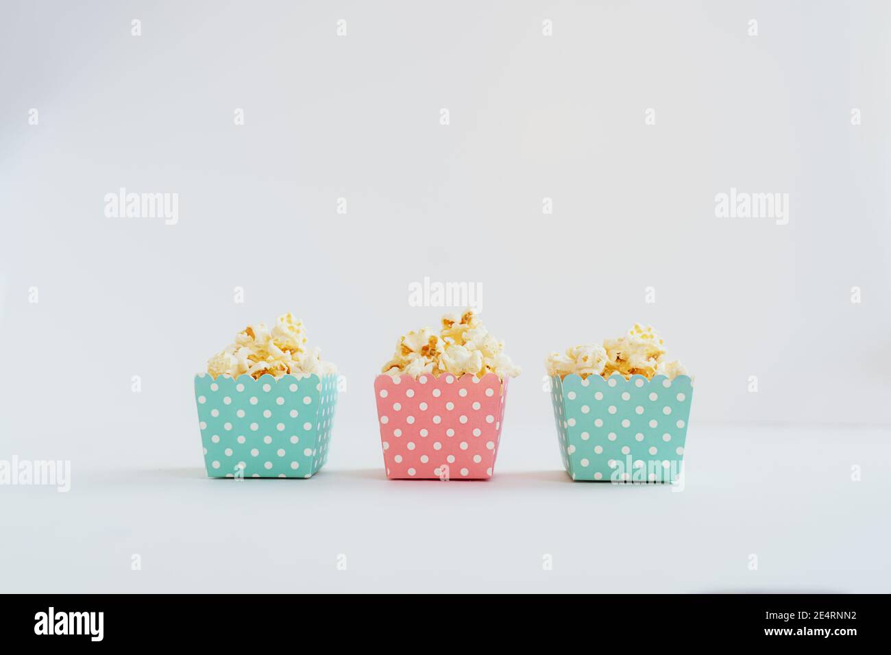 Une rangée de petites boîtes décoratives en papier bleu et rose avec pop-corn sur fond blanc. Partie enfant. Espace de copie, mise au point sélective. Banque D'Images