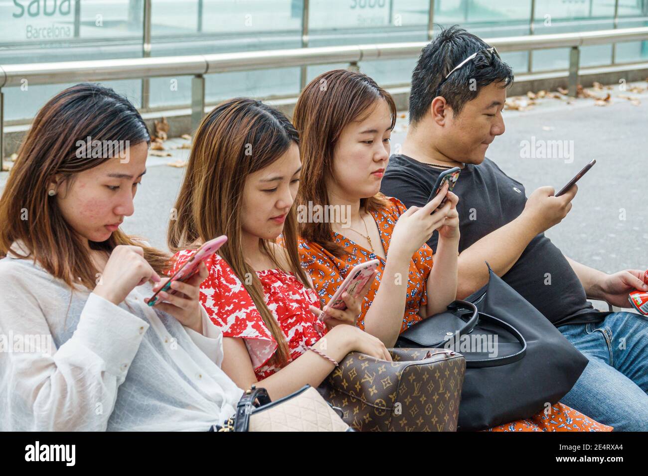 Espagne Barcelone Catalogne Catalunya Passeig de Gracia quartier des affaires banc Asiatique garçon fille adolescent adolescents adolescents assis à l'aide d'un smartphone sma Banque D'Images