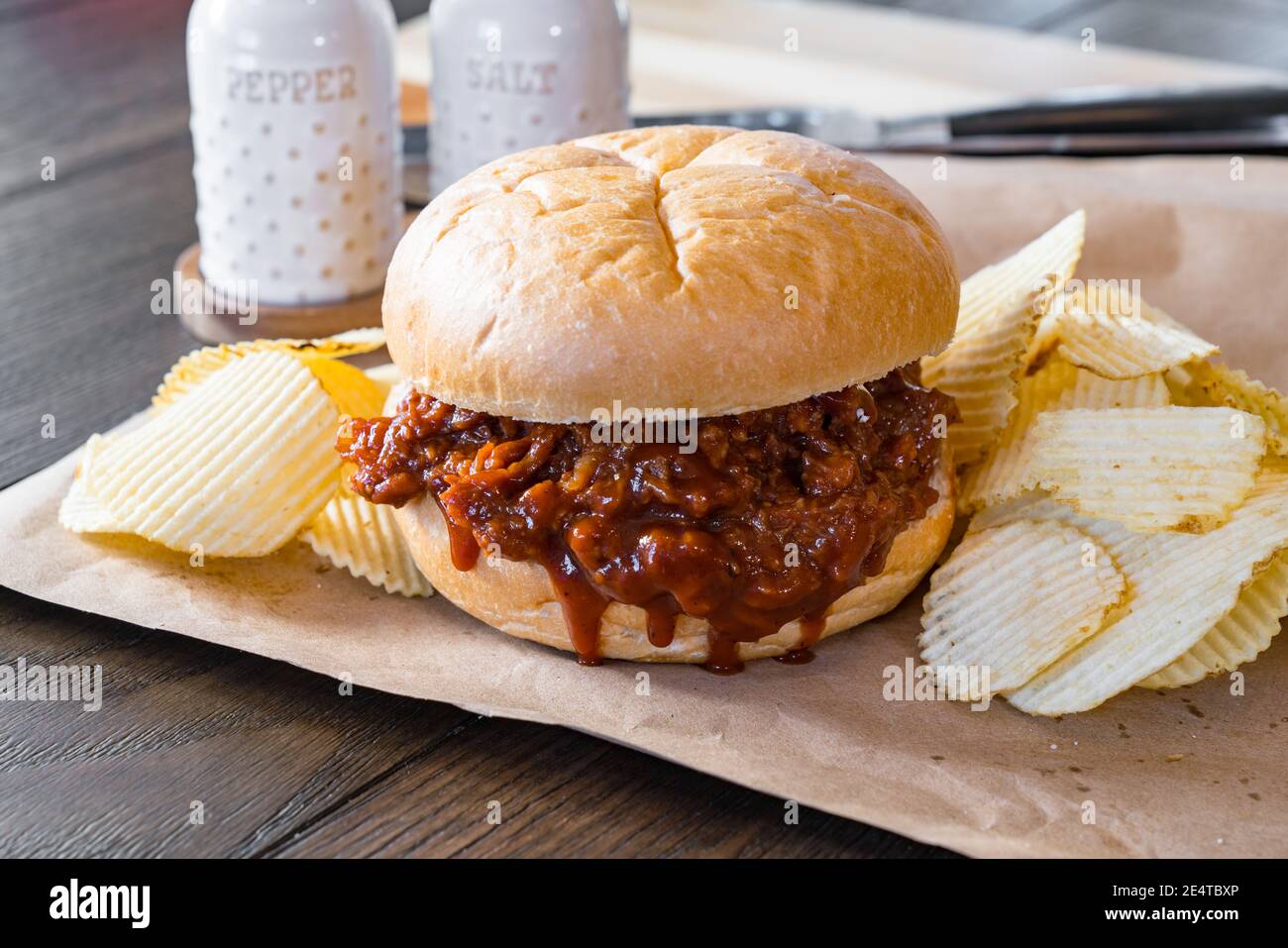 Sandwich barbecue au porc chaud et frais avec chips de pommes de terre sur papier brun Banque D'Images