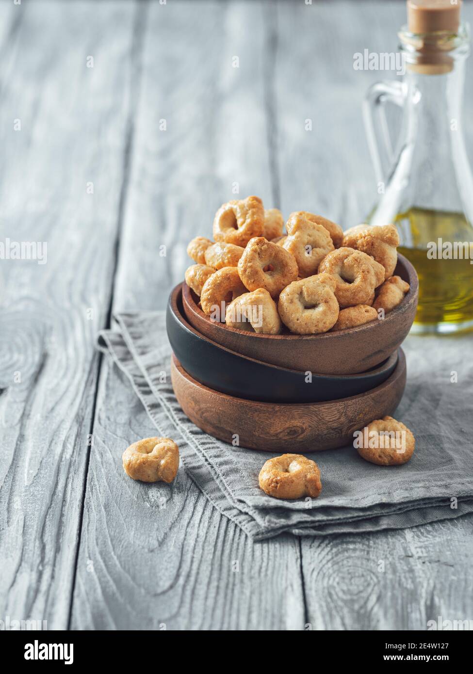 Taralli ou taralini italien traditionnel dans un bol en bois sur une ancienne table en bois grise. Photo rustique de taralli apéritif avec espace copie. Verticale. Banque D'Images
