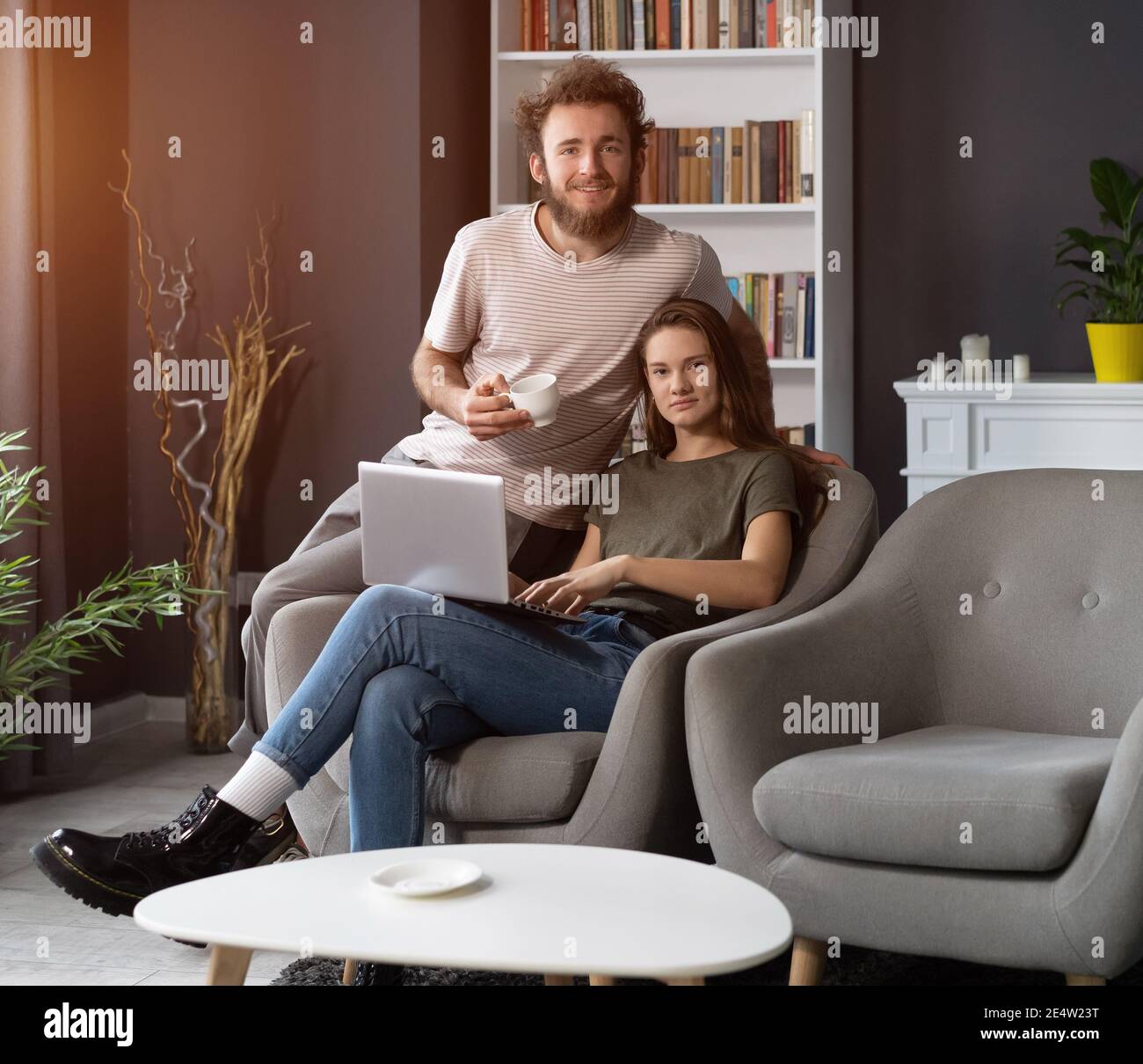 Travailler ensemble jeune couple restant en quarantaine à la maison avec assis sur les fauteuils. Un jeune couple heureux assis sur une chaise ensemble à l'aide d'un ordinateur portable Banque D'Images