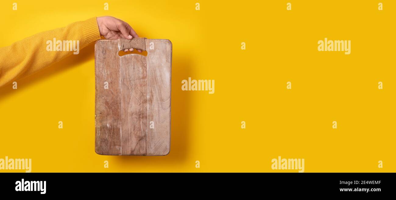 main femelle tenant une planche à découper en bois sur fond jaune Banque D'Images