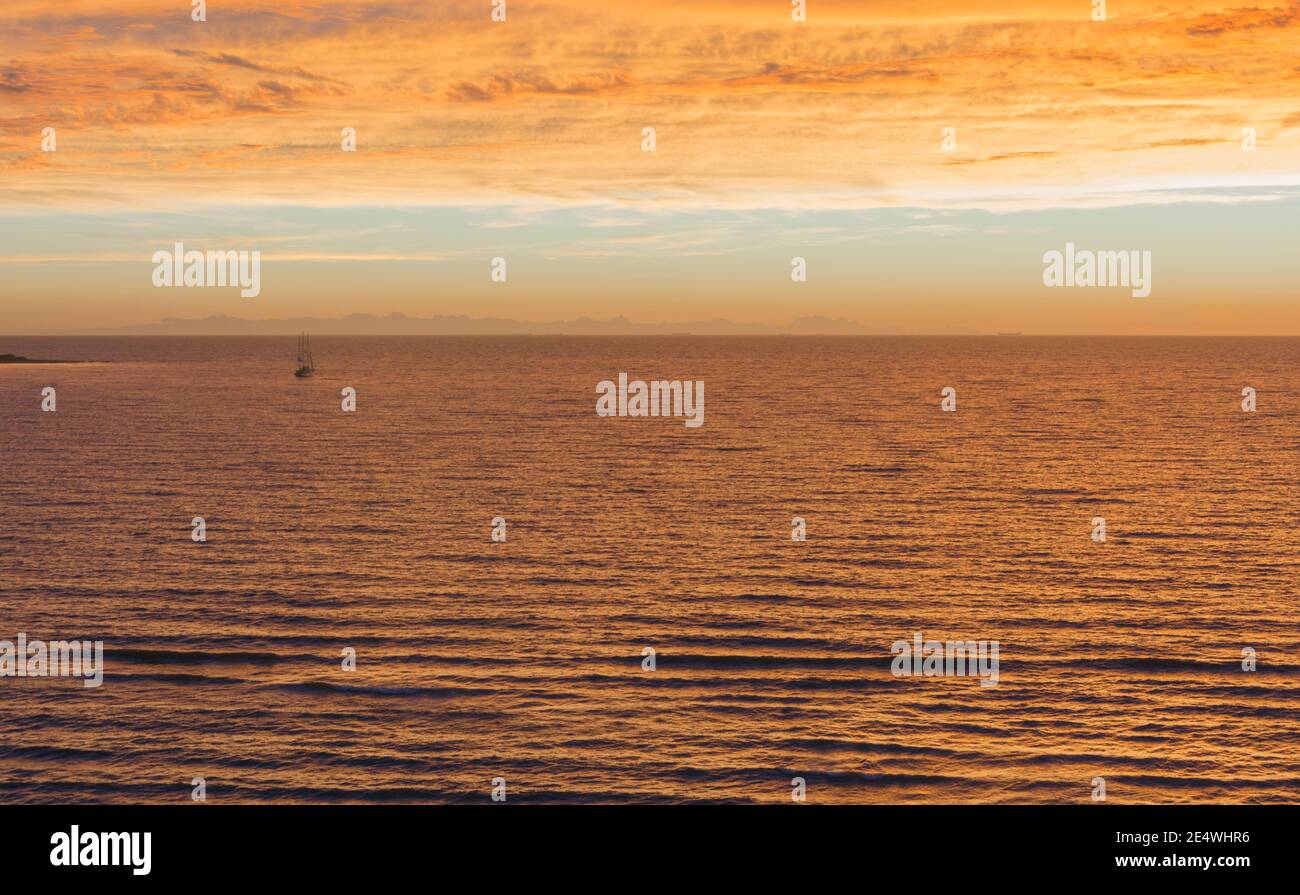 Vue sur le paysage de la mer et du ciel avec des nuages illuminés de couleurs orange et or du coucher et du lever du soleil Banque D'Images