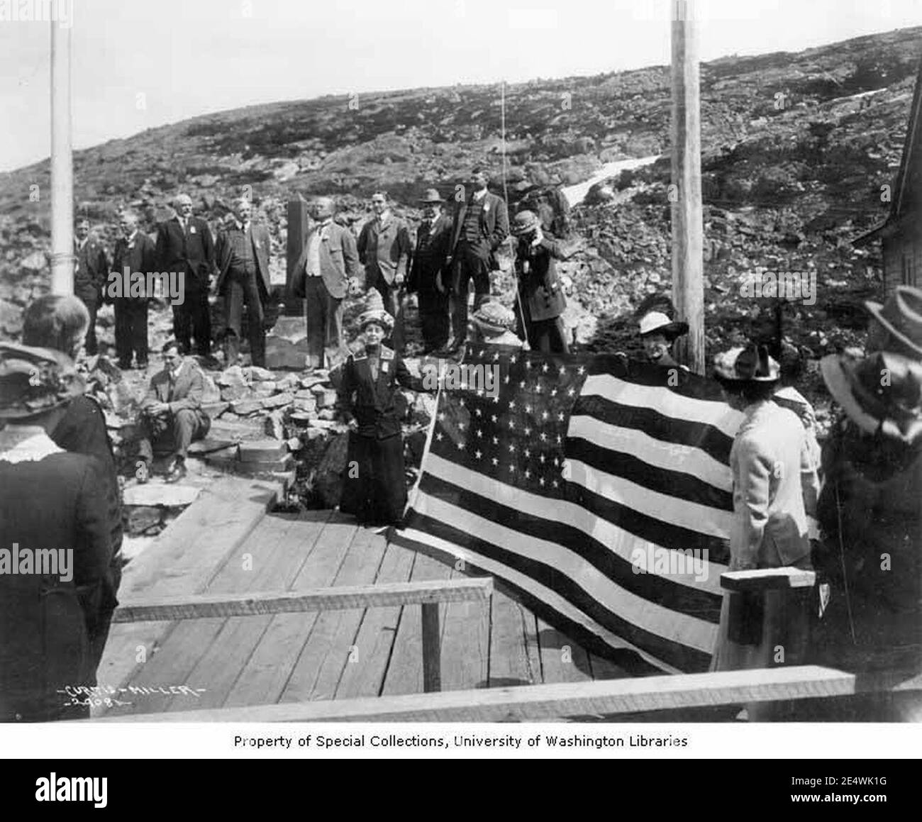 Des membres de la Chambre de commerce de Seattle qui élèvent le drapeau des États-Unis à la frontière entre l'Alaska et le Canada, vers 1914 Banque D'Images