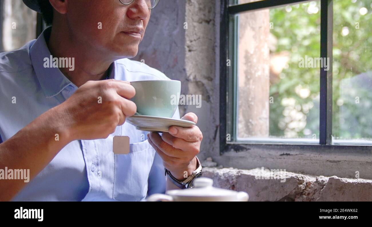 Homme adulte prenant une tasse de thé chaud dans un café. Asseyez-vous près des fenêtres. Banque D'Images