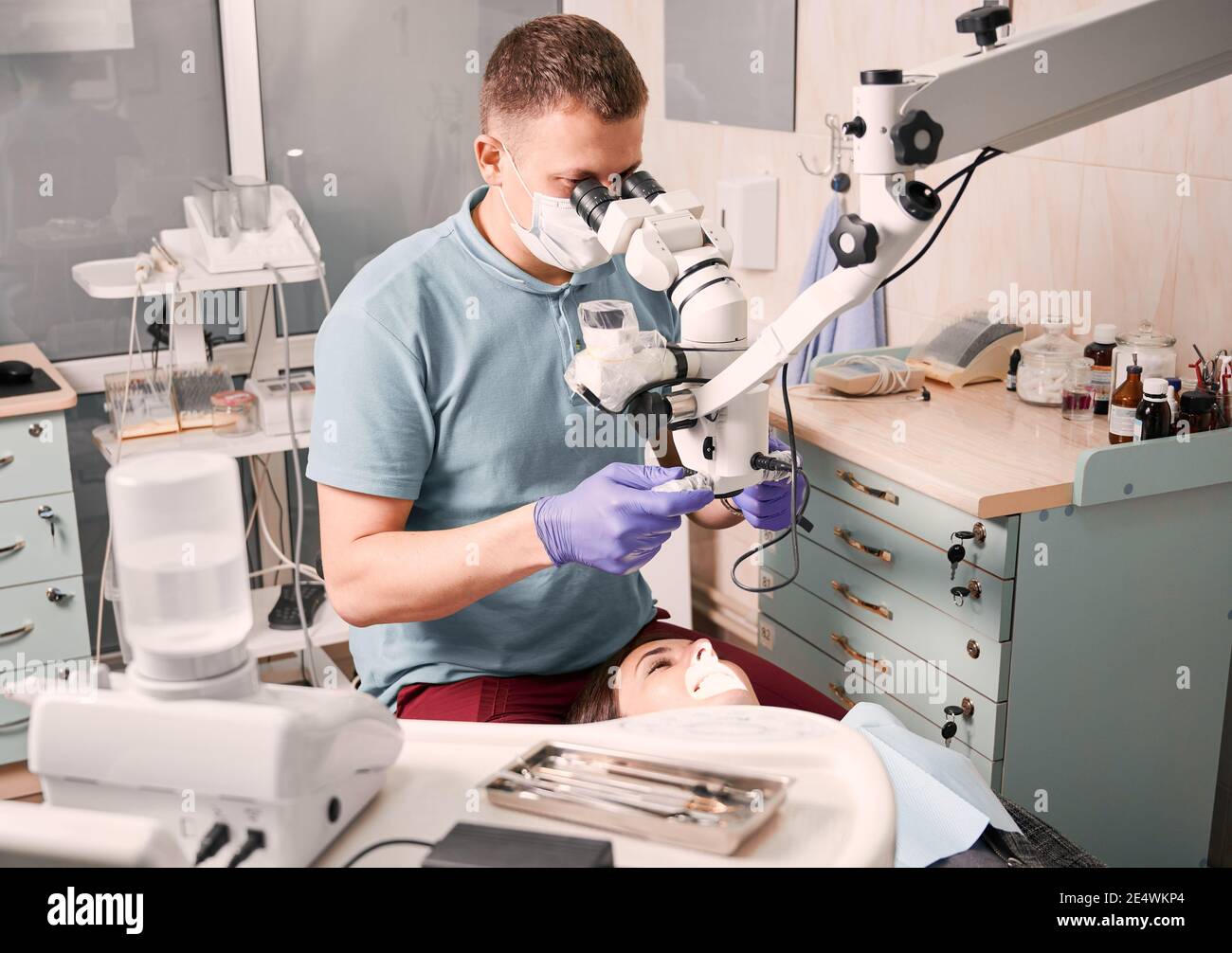 Dentiste de sexe masculin utilisant un microscope dentaire lors de la vérification des dents de la patiente. Femme allongé sur une chaise dentaire pendant que l'stomatologiste examine ses dents. Concept de la dentisterie, de la stomatologie et des soins dentaires. Banque D'Images