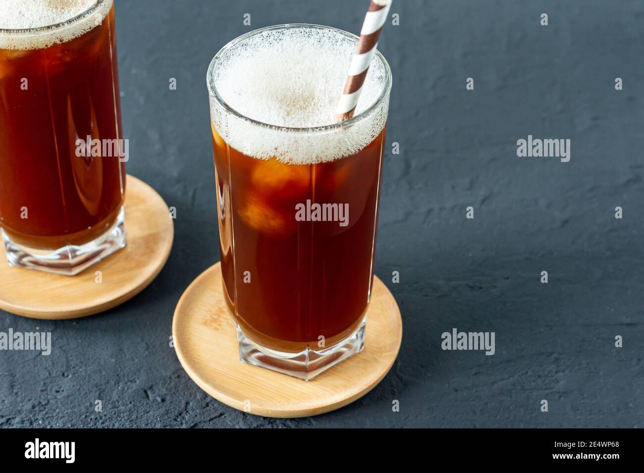 Café glacé dans de grands verres avec de la glace sur un fond en béton noir. Boisson d'été froide avec paille en papier. Banque D'Images