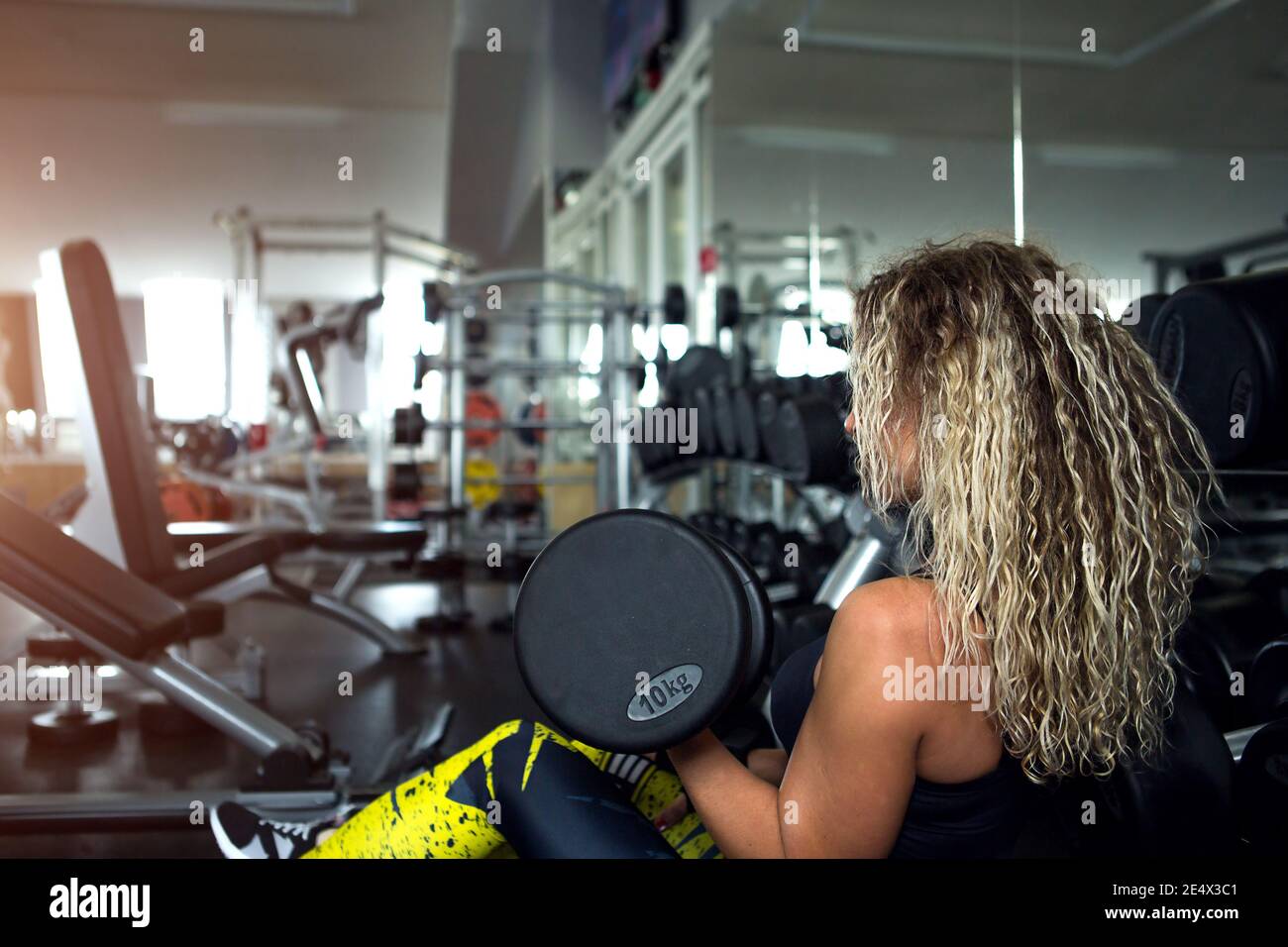 Femme aux cheveux longs et blonds bouclés tient une haltère lourde dans ses mains. Culturisme, entraîneur du club de fitness, salle de sport, vêtements de sport pour trai Banque D'Images