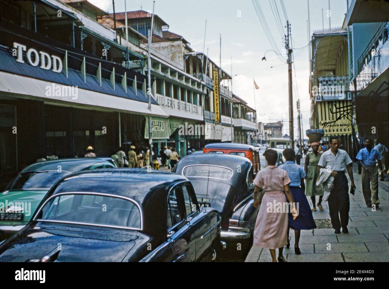 Vue sur les piétons et les vieilles voitures de Frederick Street, Port of Spain, Trinité-et-Tobago c 1958. La rue traverse la ville vers le nord dans le quartier central des affaires de la ville. Le quartier du centre-ville de Port of Spain est également le plus ancien quartier de la ville. Frederick Street a présenté une architecture coloniale traditionnelle et quelques boutiques anciennes célèbres, comme les magasins Miller's, Todd et Hendinning ici. Cette image provient d'une transparence de couleur 35 mm amateur ancienne. Banque D'Images