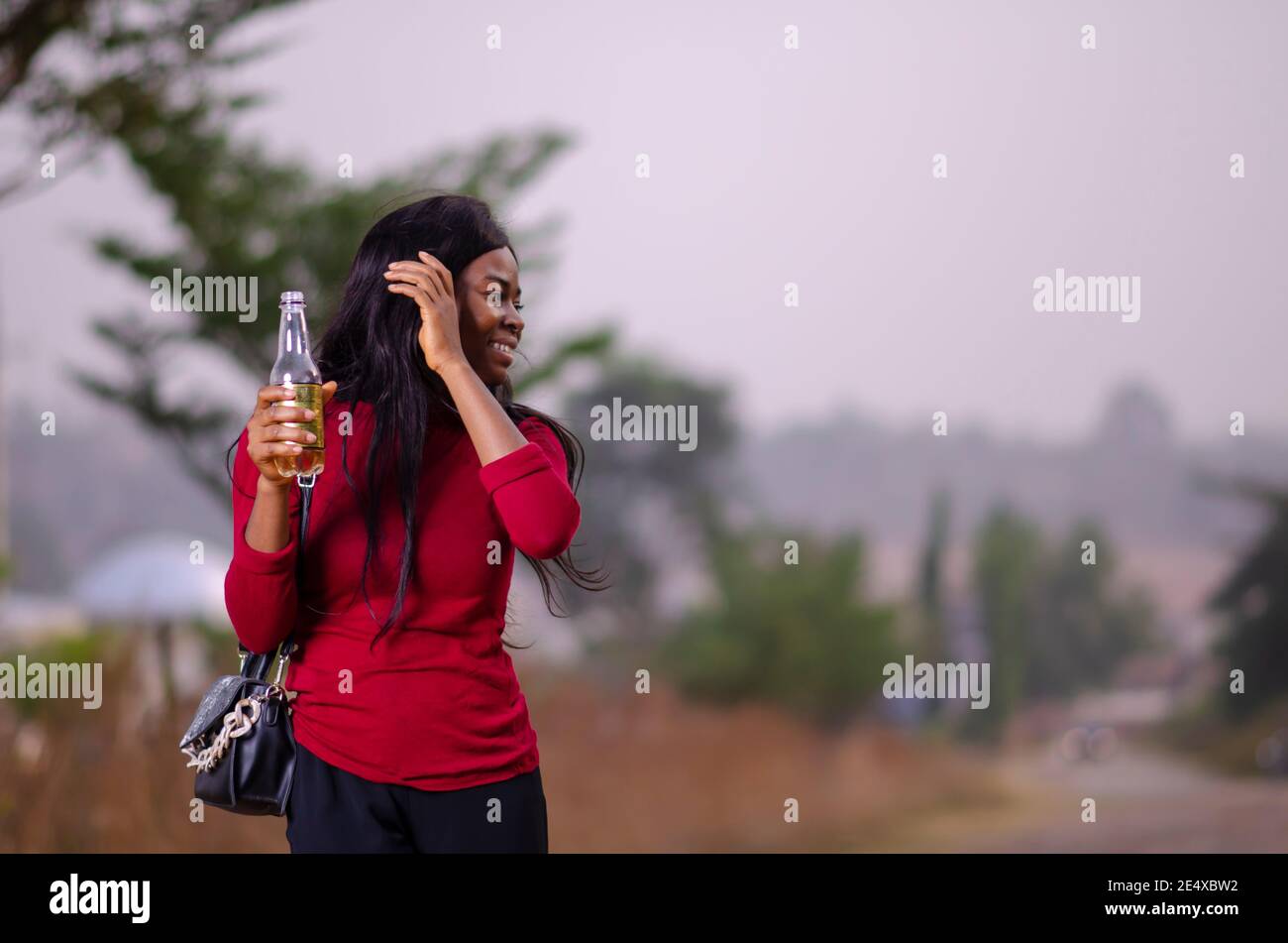 jeune belle femme africaine debout dans un jardin et tenue une bouteille de boisson Banque D'Images