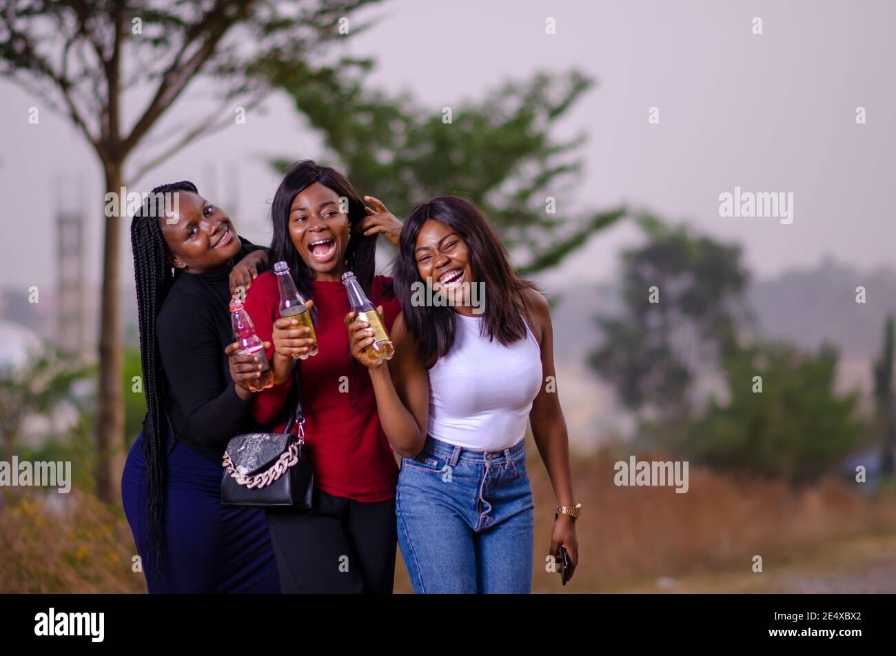 jeunes belles femmes africaines qui se promènent dans un jardin, qui tiennent des bouteilles de boisson et qui ont une bonne discussion Banque D'Images