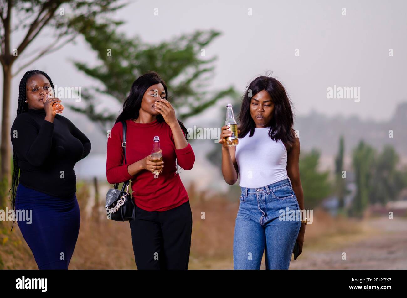 jeunes belles femmes africaines qui se promènent dans un jardin, qui tiennent des bouteilles de boisson et qui ont une bonne discussion Banque D'Images