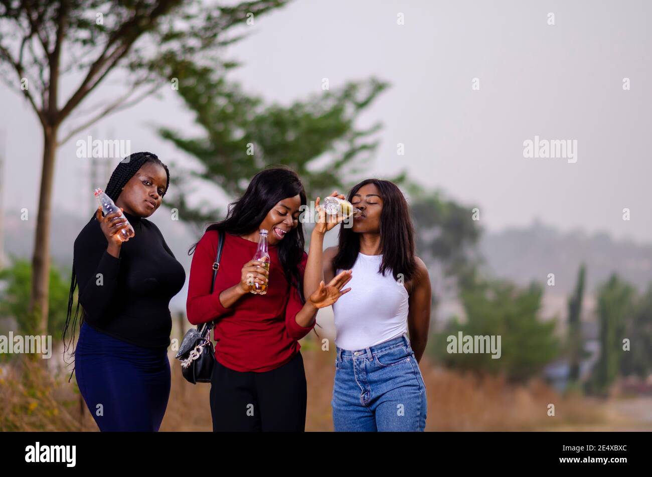 jeunes belles femmes africaines qui se promènent dans un jardin, qui tiennent des bouteilles de boisson et qui ont une bonne discussion Banque D'Images