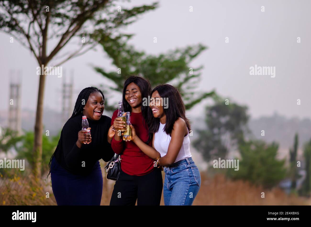 jeunes belles femmes africaines qui se promènent dans un jardin, qui tiennent des bouteilles de boisson et qui ont une bonne discussion Banque D'Images