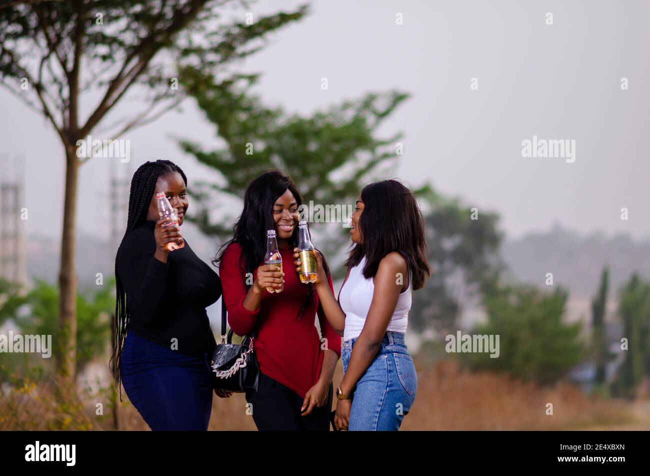 jeunes belles femmes africaines qui se promènent dans un jardin, qui tiennent des bouteilles de boisson et qui ont une bonne discussion Banque D'Images