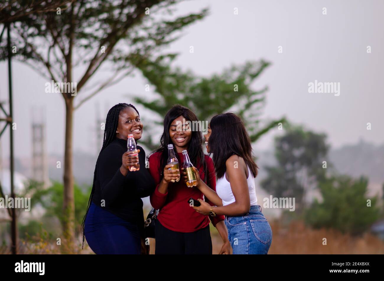 jeunes belles femmes africaines qui se promènent dans un jardin, qui tiennent des bouteilles de boisson et qui ont une bonne discussion Banque D'Images