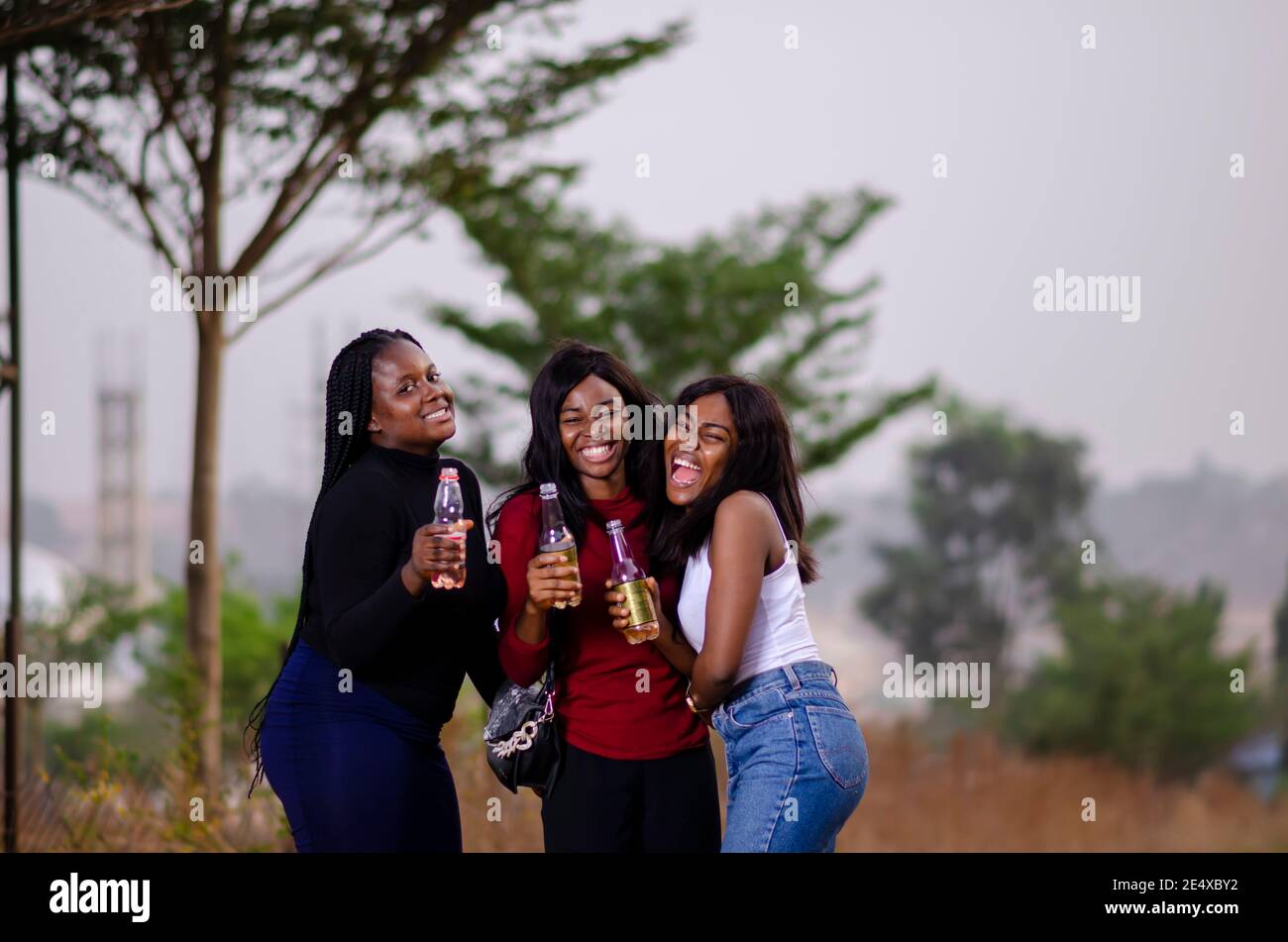 jeunes belles femmes africaines qui se promènent dans un jardin, qui tiennent des bouteilles de boisson et qui ont une bonne discussion Banque D'Images