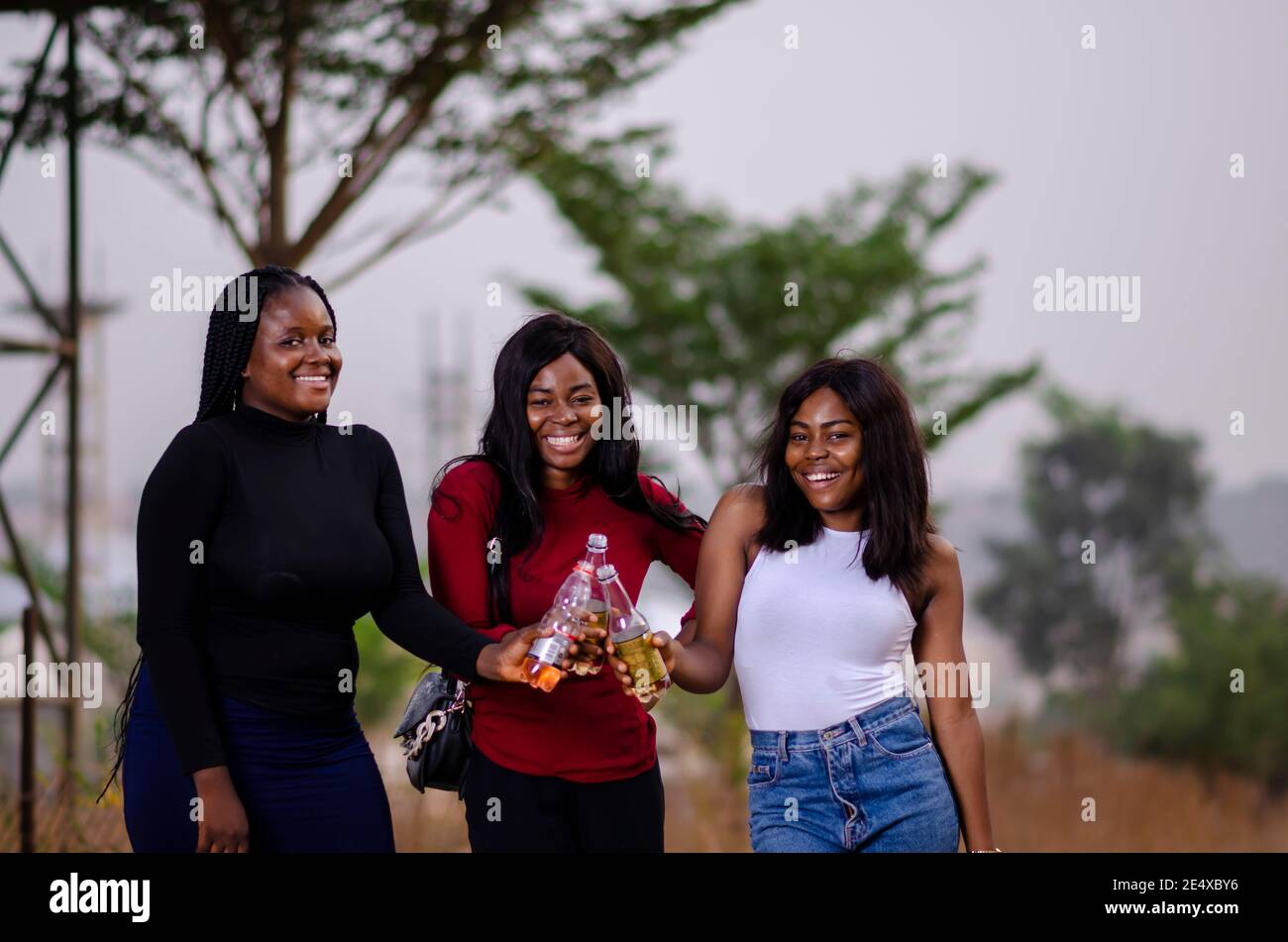 jeunes belles femmes africaines qui se promènent dans un jardin, qui tiennent des bouteilles de boisson et qui ont une bonne discussion Banque D'Images