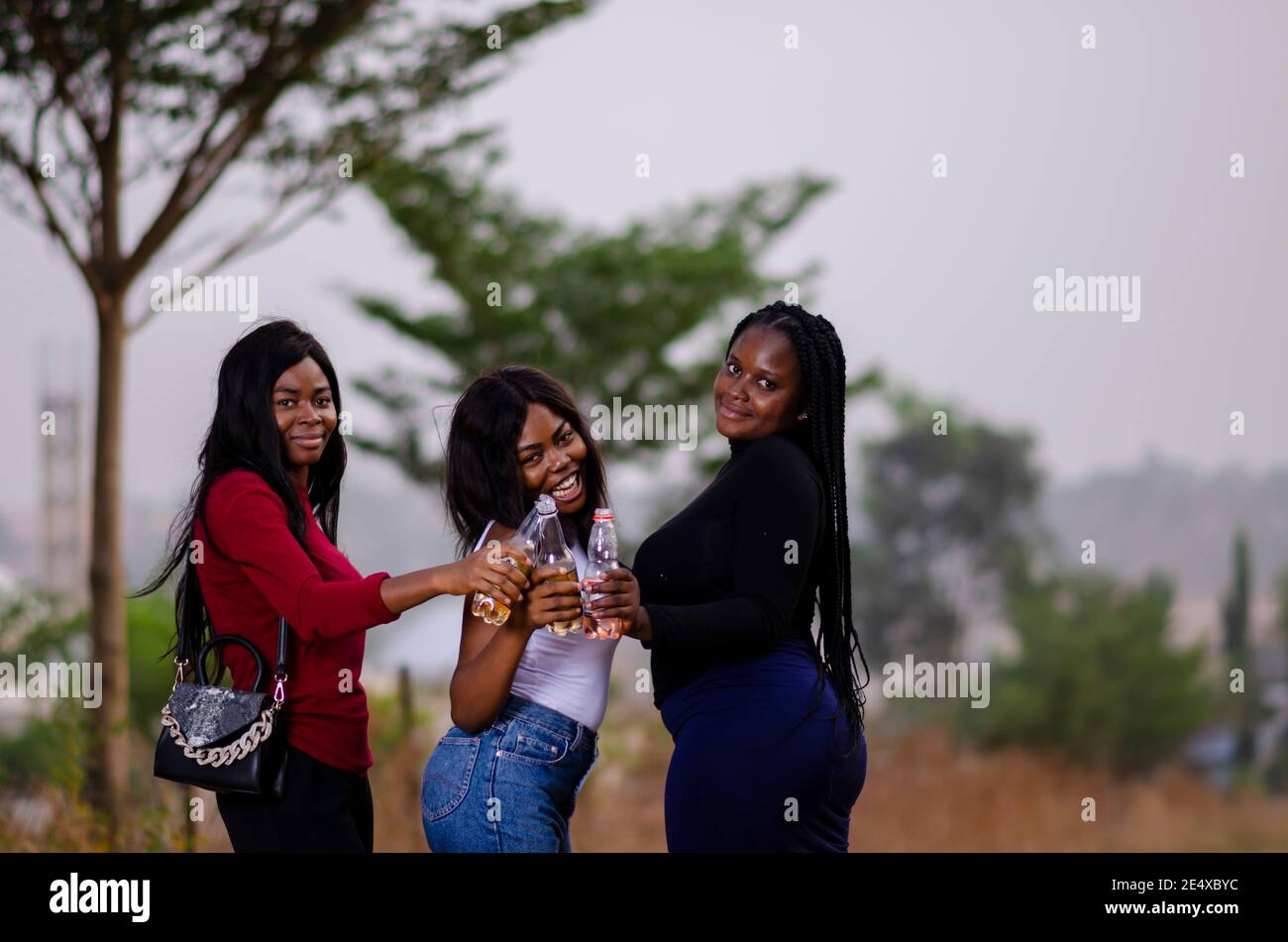 jeunes belles femmes africaines qui se promènent dans un jardin, qui tiennent des bouteilles de boisson et qui ont une bonne discussion Banque D'Images