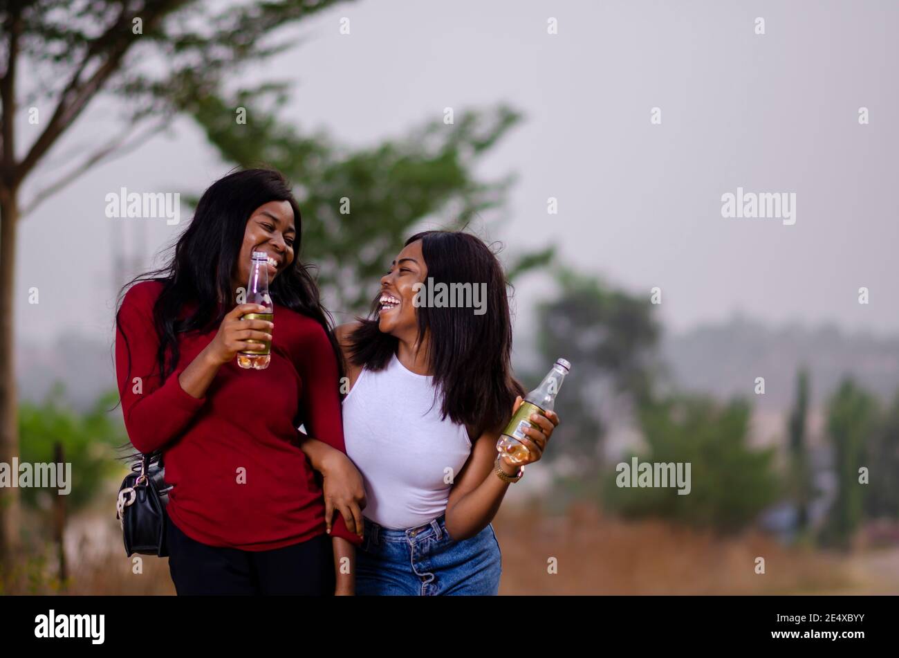 jeunes belles femmes africaines qui se promènent dans un jardin, qui tiennent des bouteilles de boisson et qui ont une bonne discussion Banque D'Images