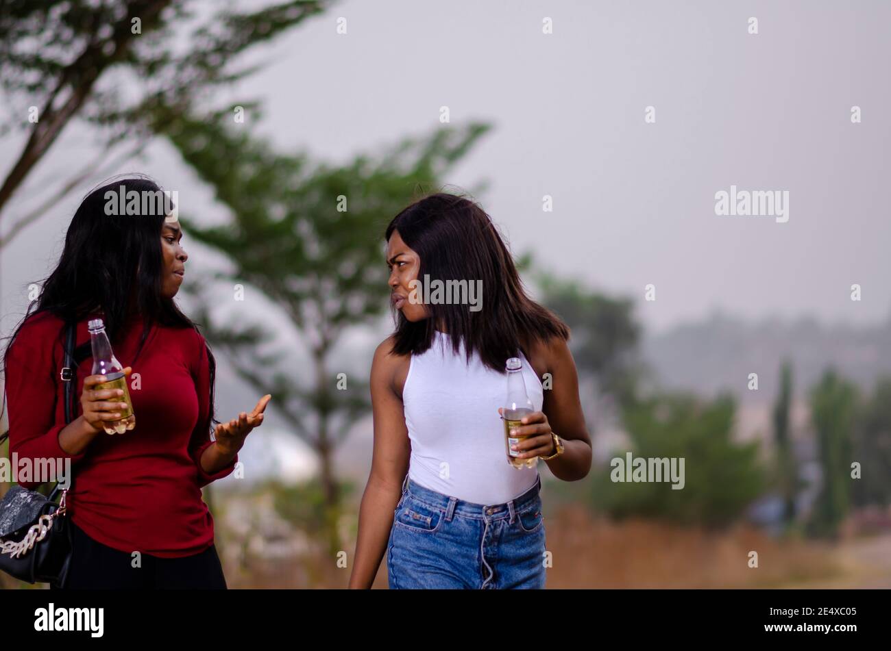 jeunes belles femmes africaines qui se promènent dans un jardin, qui tiennent des bouteilles de boisson et qui ont une bonne discussion Banque D'Images