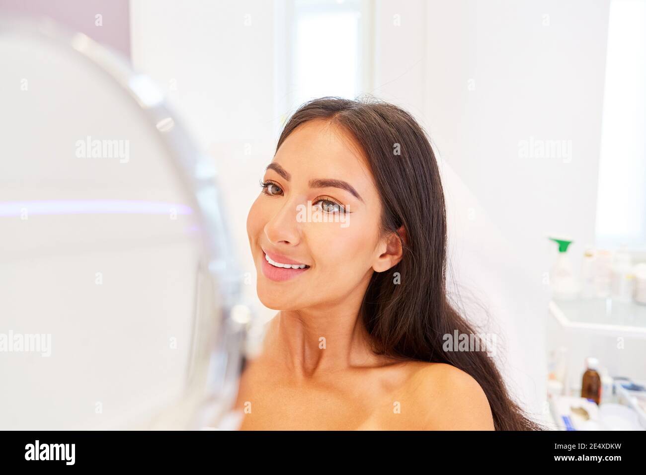 Une jeune femme souriante regarde son visage dans le miroir après une chirurgie plastique Banque D'Images
