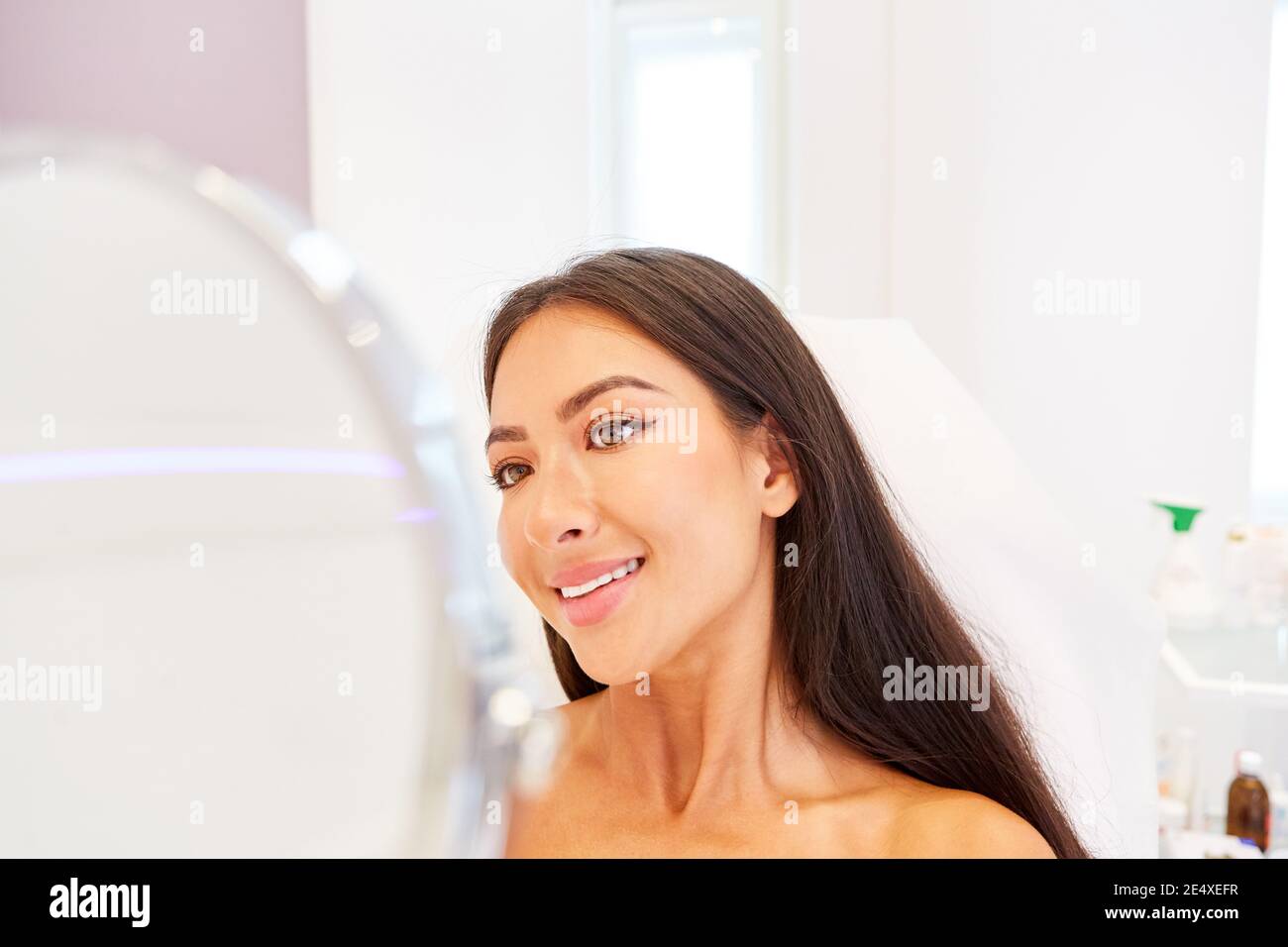 Une femme heureuse regarde son visage dans le miroir après chirurgie esthétique réussie Banque D'Images