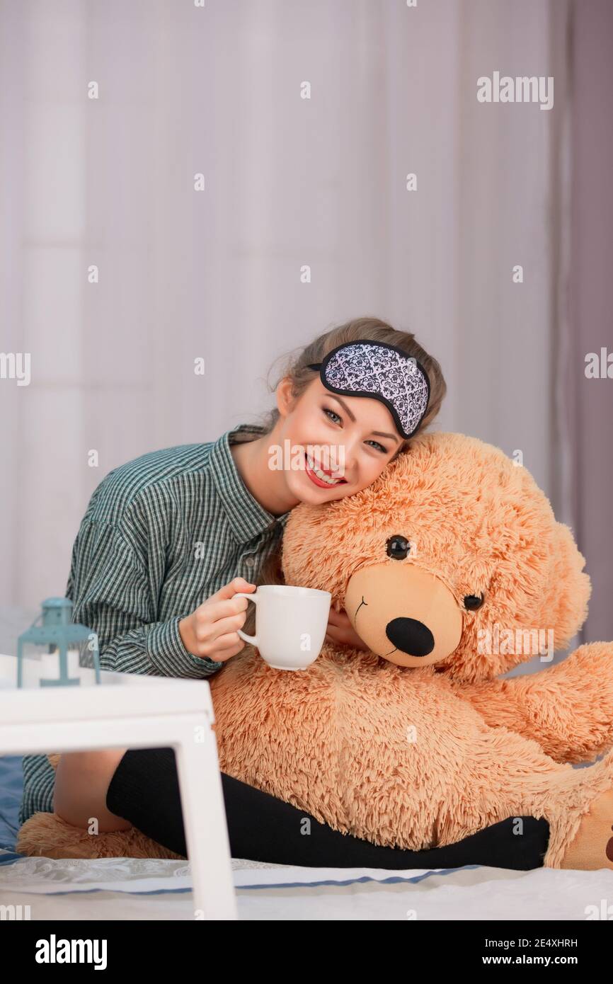 Petit déjeuner au lit. Une jeune femme sourit, boit du thé au café et tue un grand ours en peluche. Photo de haute qualité Banque D'Images