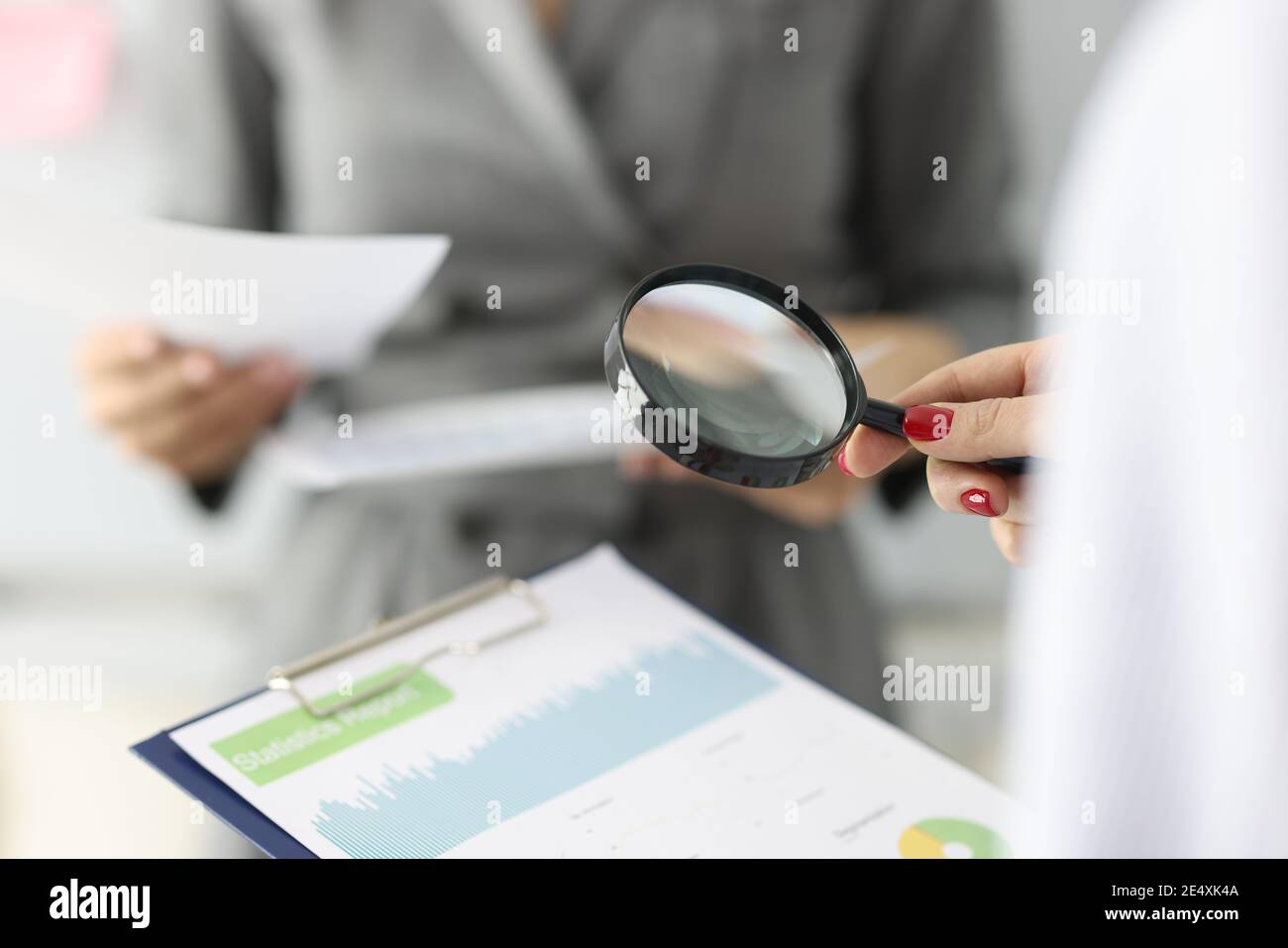 La main femelle tient une loupe et un presse-papiers avec des chiffres financiers Banque D'Images