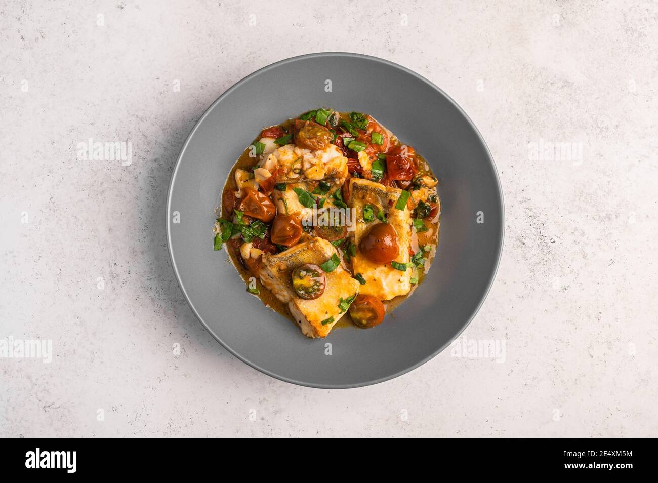 Poisson sicilien traditionnel avec tomates, olives, persil et poivre rouge dans une assiette profonde sur fond clair, vue du dessus Banque D'Images