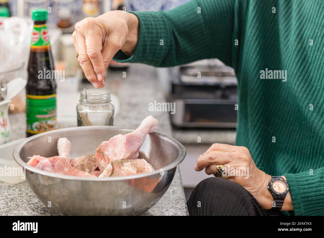 Femme âgée mettant du poivre à la main sur des pilons de poulet. Banque D'Images