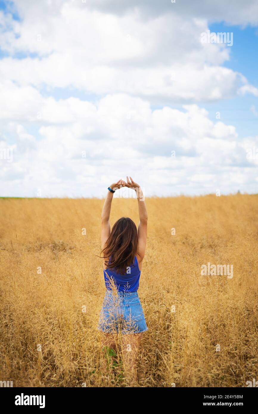 Portrait d'une jeune belle femme brune dans un t-shirt bleu et un short en denim se tient au milieu du champ, exposant son visage au soleil sur le Banque D'Images