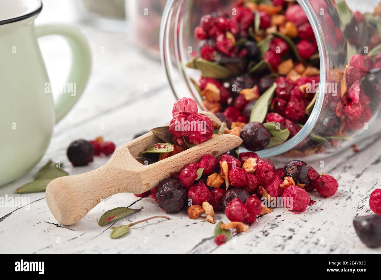 Pot en verre de thé aux fruits avec pommes, baies de cassis, orange et rouge, gros plan sur une table de cuisine blanche. Banque D'Images
