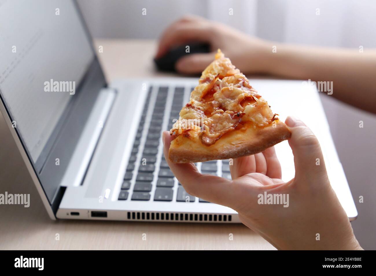 Fille mangeant de la pizza pendant le travail à l'ordinateur portable, main de femme gros vers le haut. Encas au bureau, restauration rapide Banque D'Images