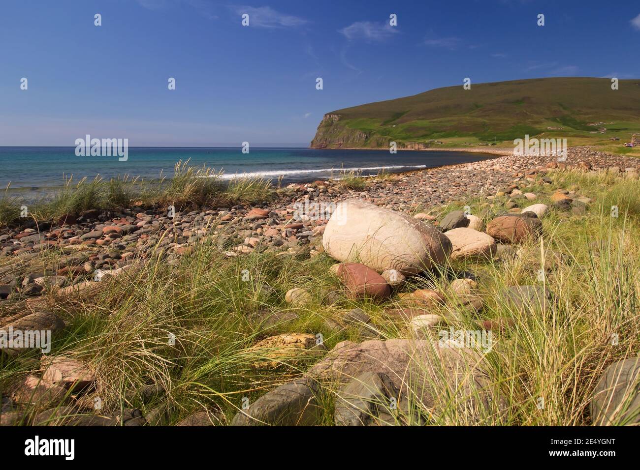 Grandes pierres rondes sur la plage écossaise pittoresque avec des falaises vertes Au loin sur les îles écossaises d'Orkney l'été midi Banque D'Images