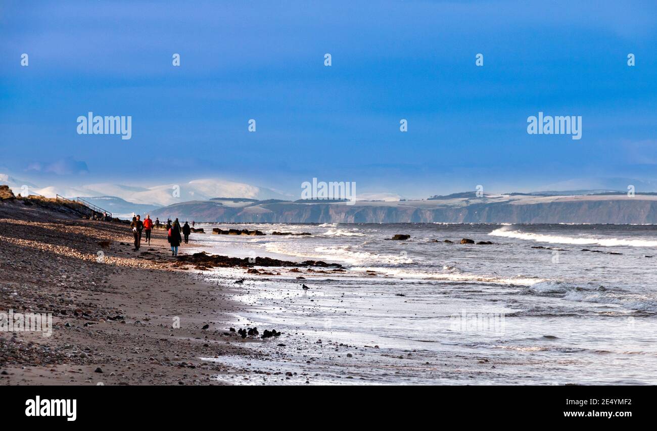 MORAY COAST SCOTLAND WINTER BEACH SCENE AVEC RANDONNEURS AHD JOGGEURS NEIGE SUR LES MONTAGNES DE L'ÎLE NOIRE AU LOIN Banque D'Images