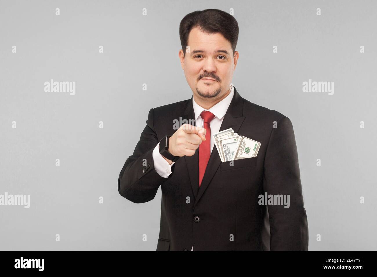 Beau homme d'affaires pointant le doigt vers l'appareil photo avec un petit sourire. Prise de vue en studio en intérieur, isolée sur fond gris Banque D'Images