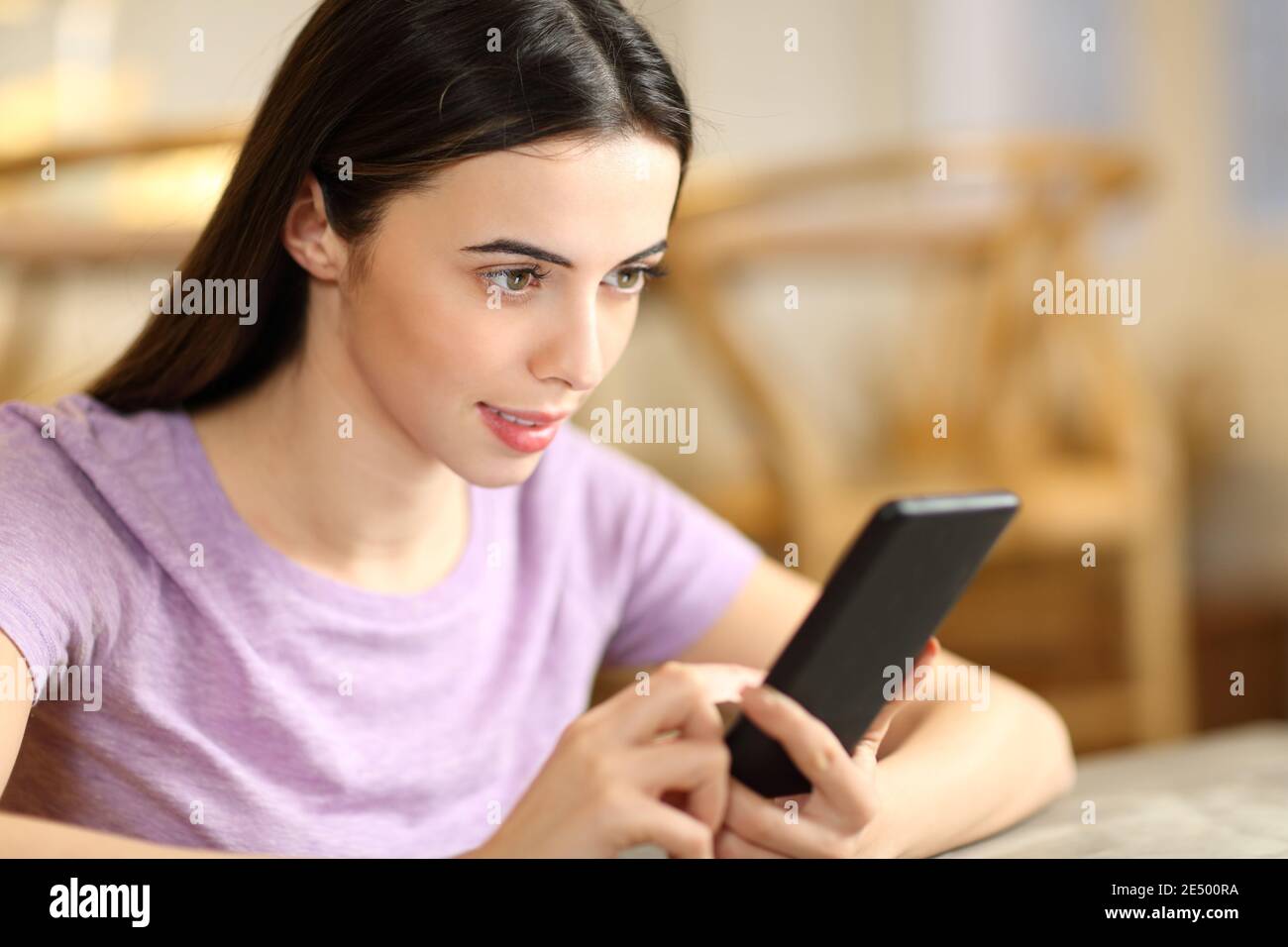 Femme concentrée vérifiant le contenu sur un smartphone assis à la maison Banque D'Images
