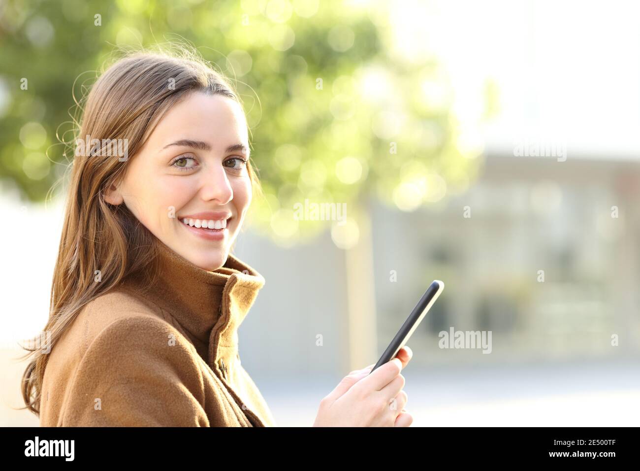 Une femme heureuse tenant un téléphone portable vous regarde en hiver dans la rue Banque D'Images