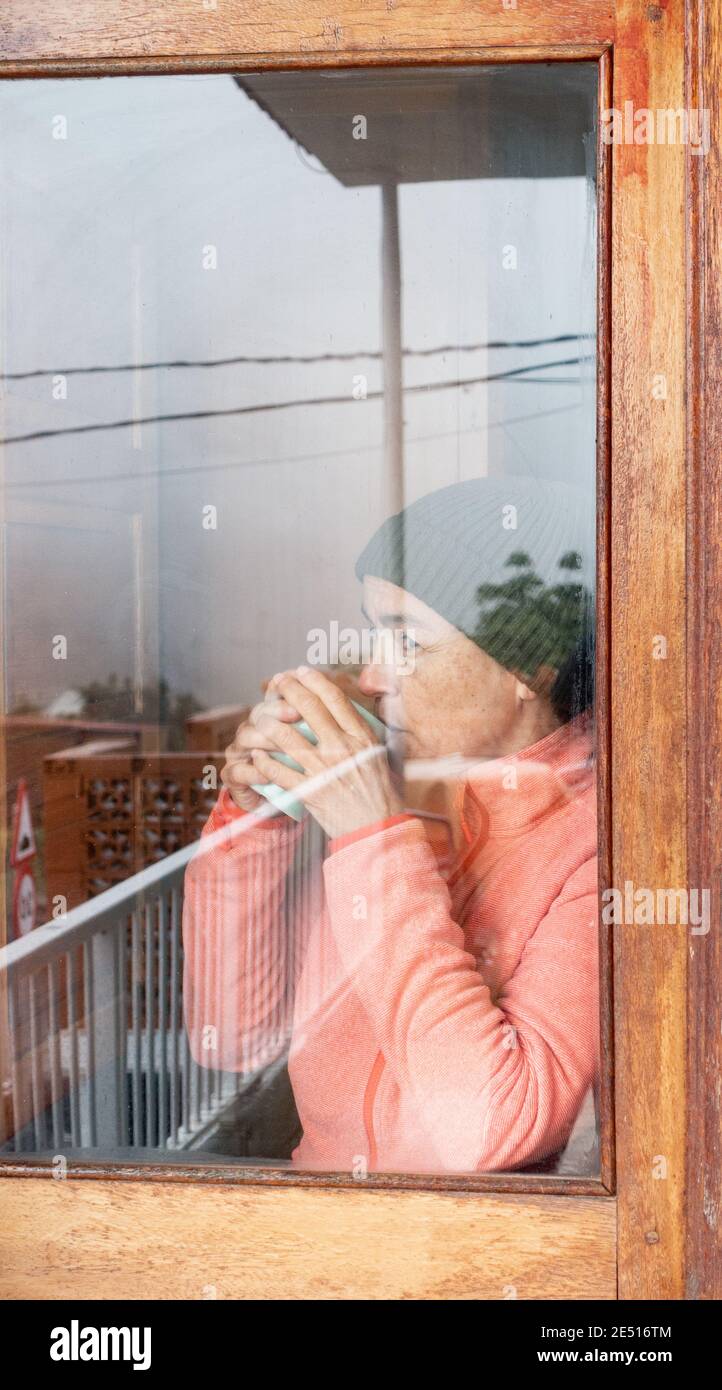 Femme d'âge moyen avec une tasse de café regardant par la fenêtre un jour froid. Banque D'Images