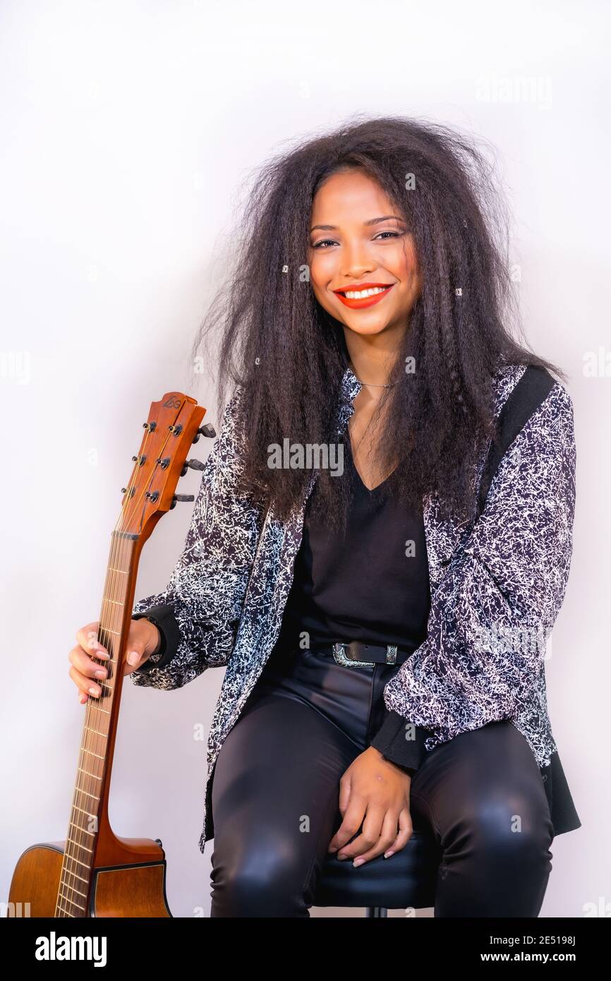 Portrait vertical d'une musicienne joyeuse assise sur un et tenir une guitare acoustique Banque D'Images