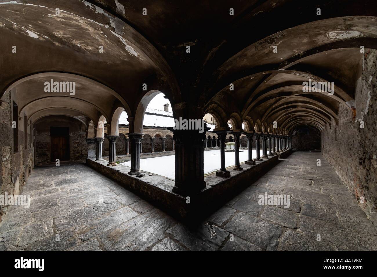 Vue symétrique grand angle d'un cloître médiéval en pierre noire du nord de l'Italie, avec des arcs ronds et des colonnes appariées Banque D'Images