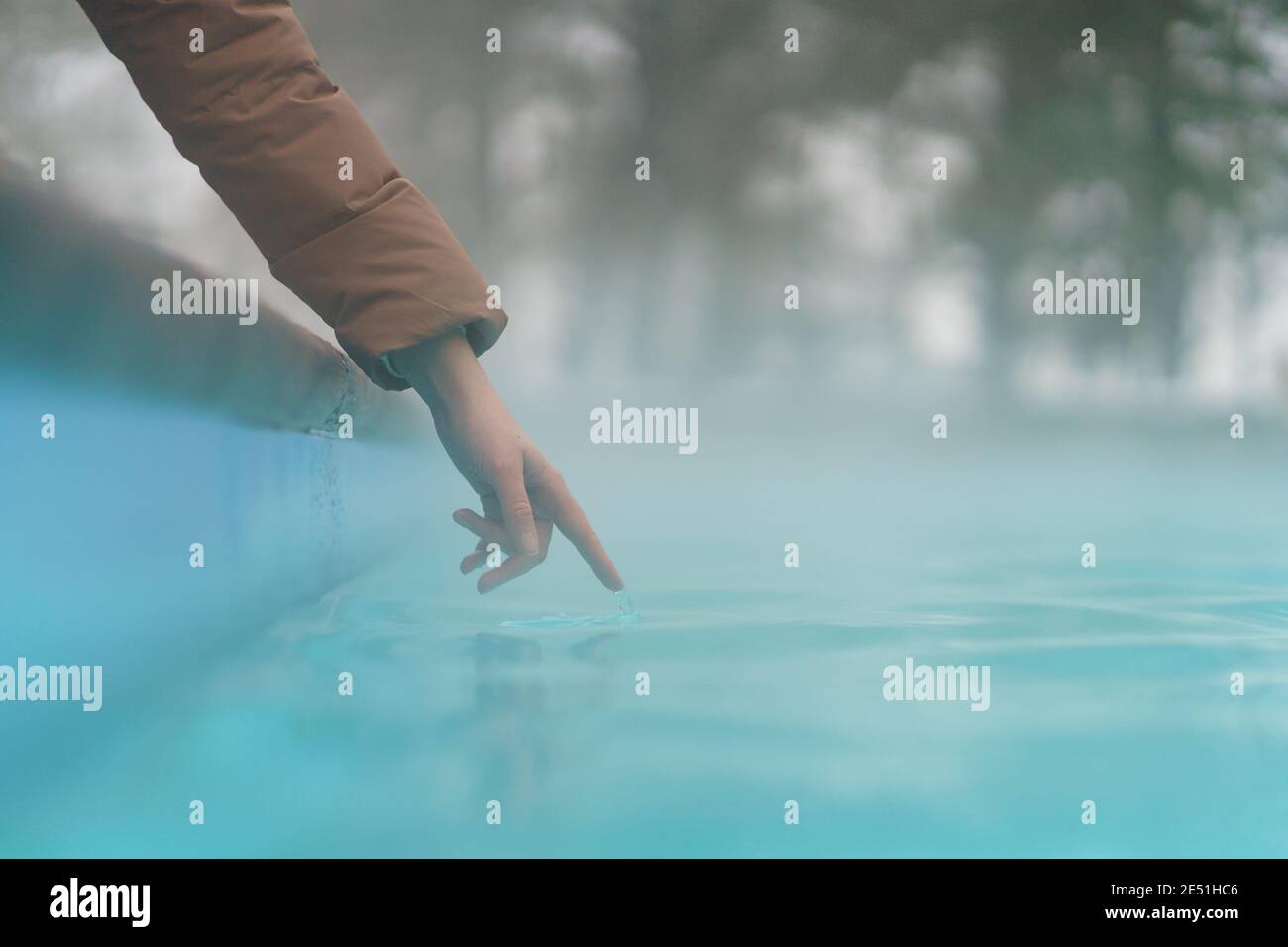 Main de femme vérifiant la température de l'eau dans la piscine ouverte en hiver. Bain bouillonnant extérieur. Banque D'Images