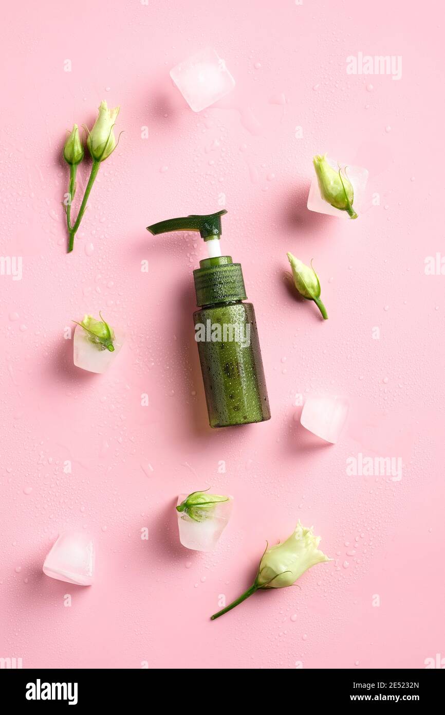Bouteille de gel douche vert, glaçons et fleurs sur fond rose. Flat lay, vue de dessus. Banque D'Images